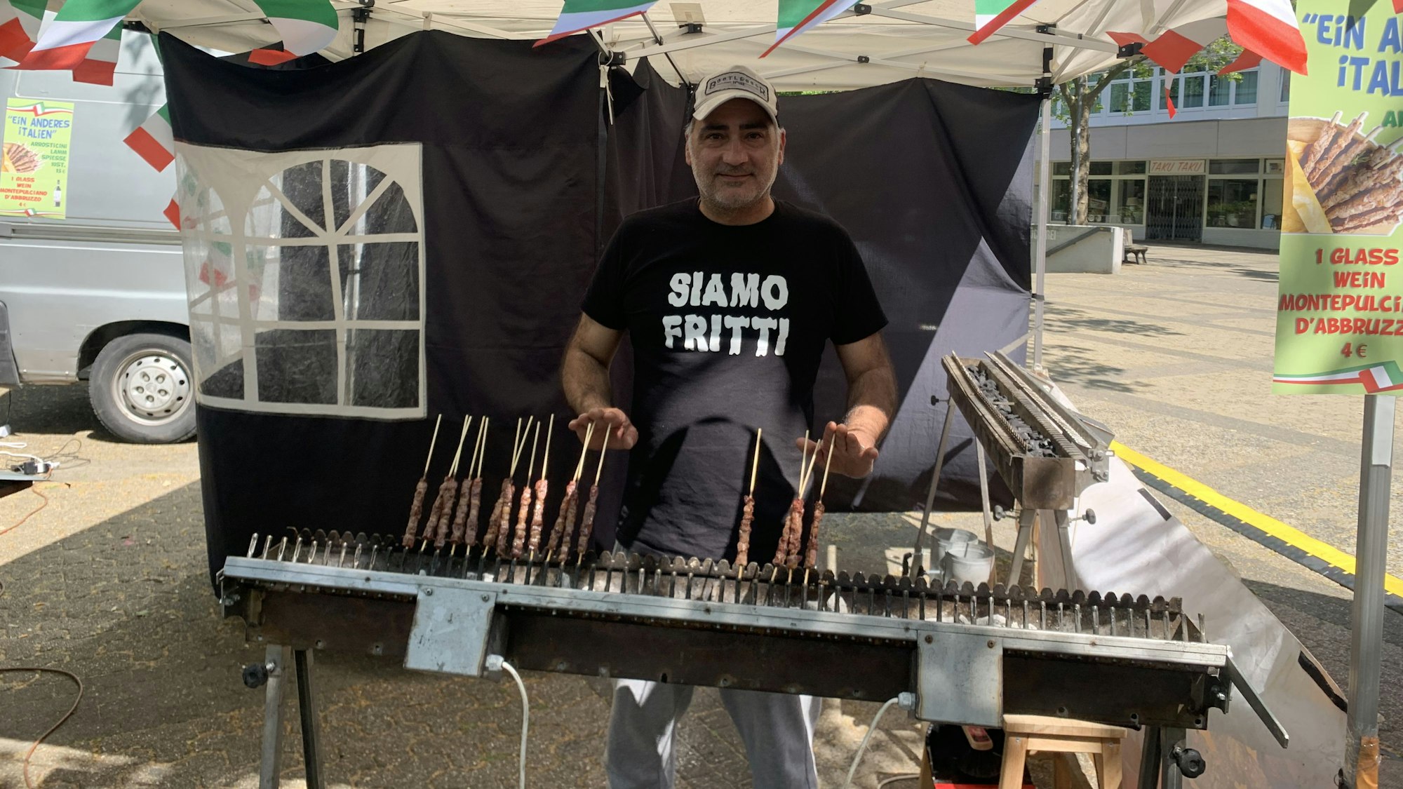 Auf dem Foto ist ein Mann zu sehen, der auf einem Grill Fleischspieße zubereitet.