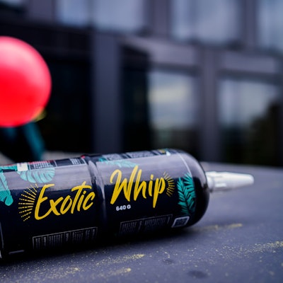Eine Flasche Lachgas, im Hintergrund hat eine junge Person einen vollen Luftballon am Mund