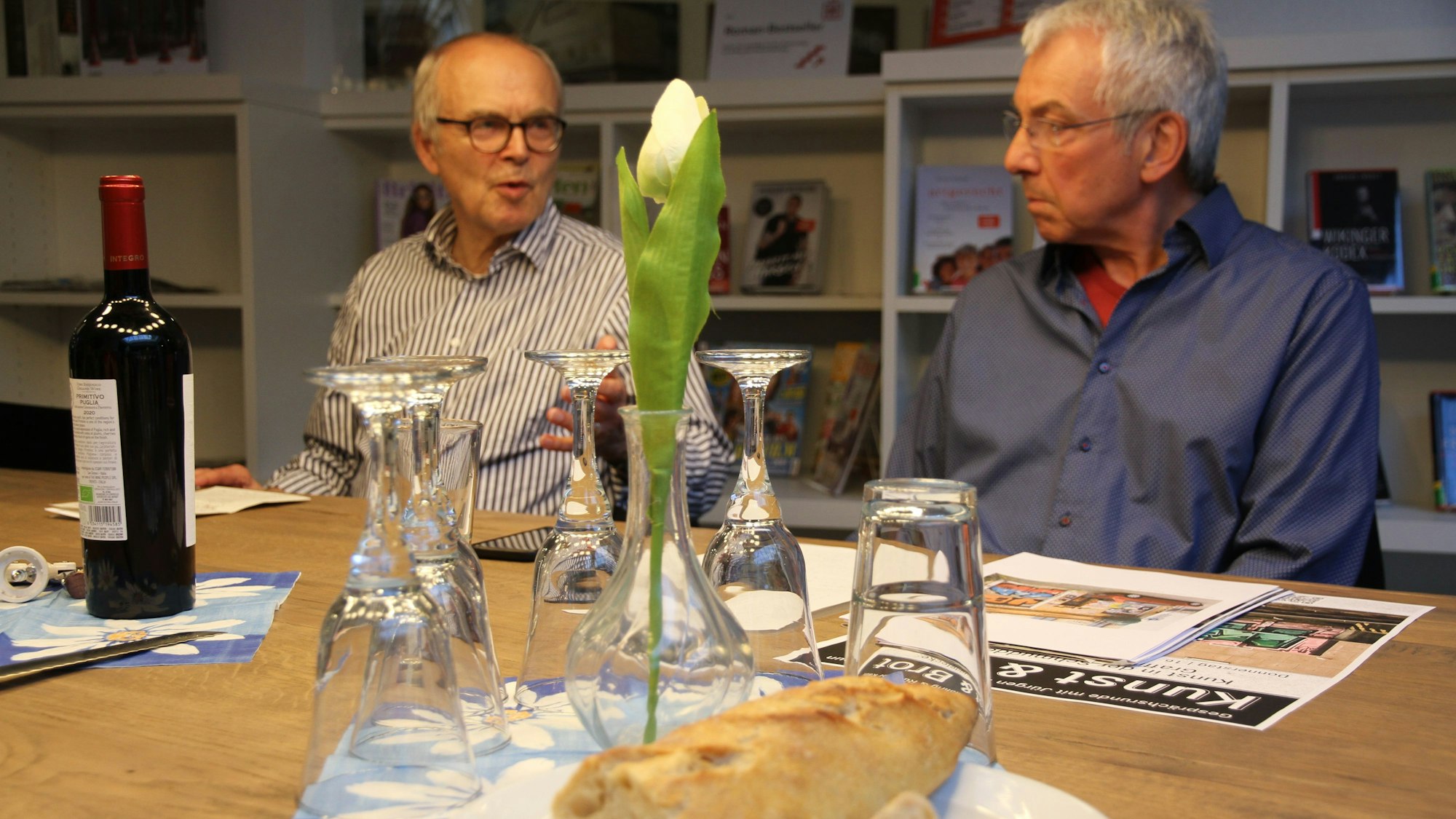 Zwei Männer an einem Tisch mit Trinkgläsern und Brot.