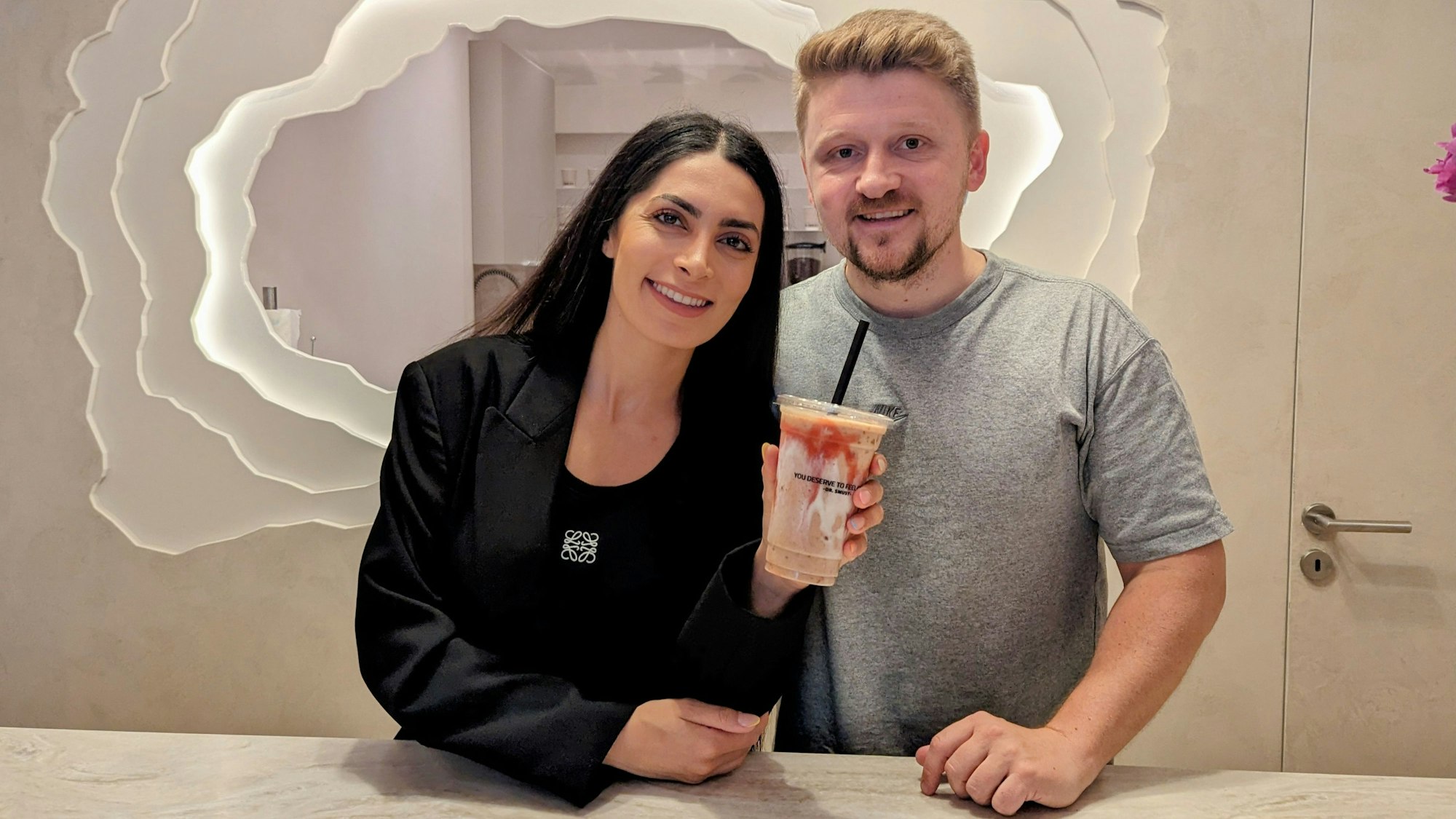 Eine Frau und ein Mann schauen in die Kamera, die Frau hält einen Smoothie in der Hand.