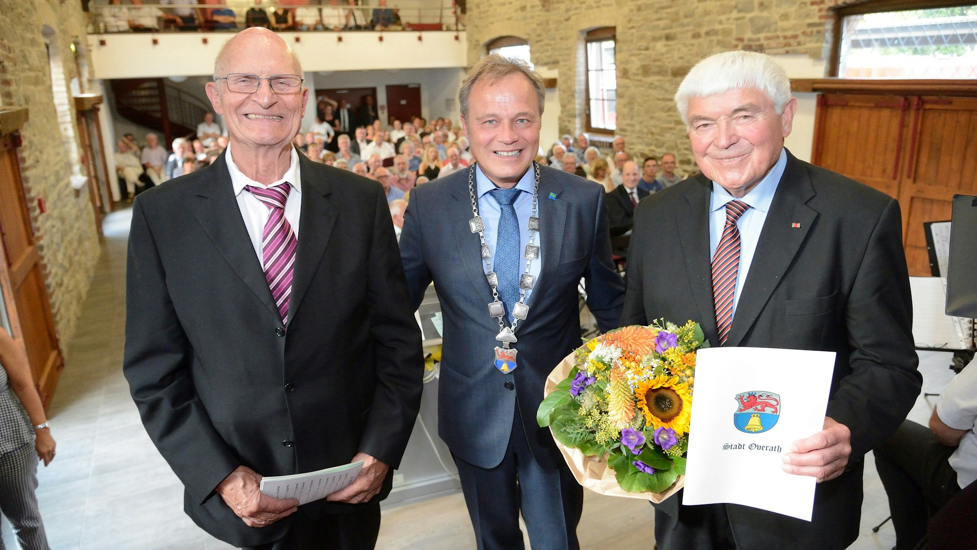 Die Overather Ehrenbürger Siegfried Raimann und Norbert Kuhl stehen mit Bürgermeister Jörg Weigt im Jahr 2018 auf der Bühne des Kulturbahnhofs Overath.