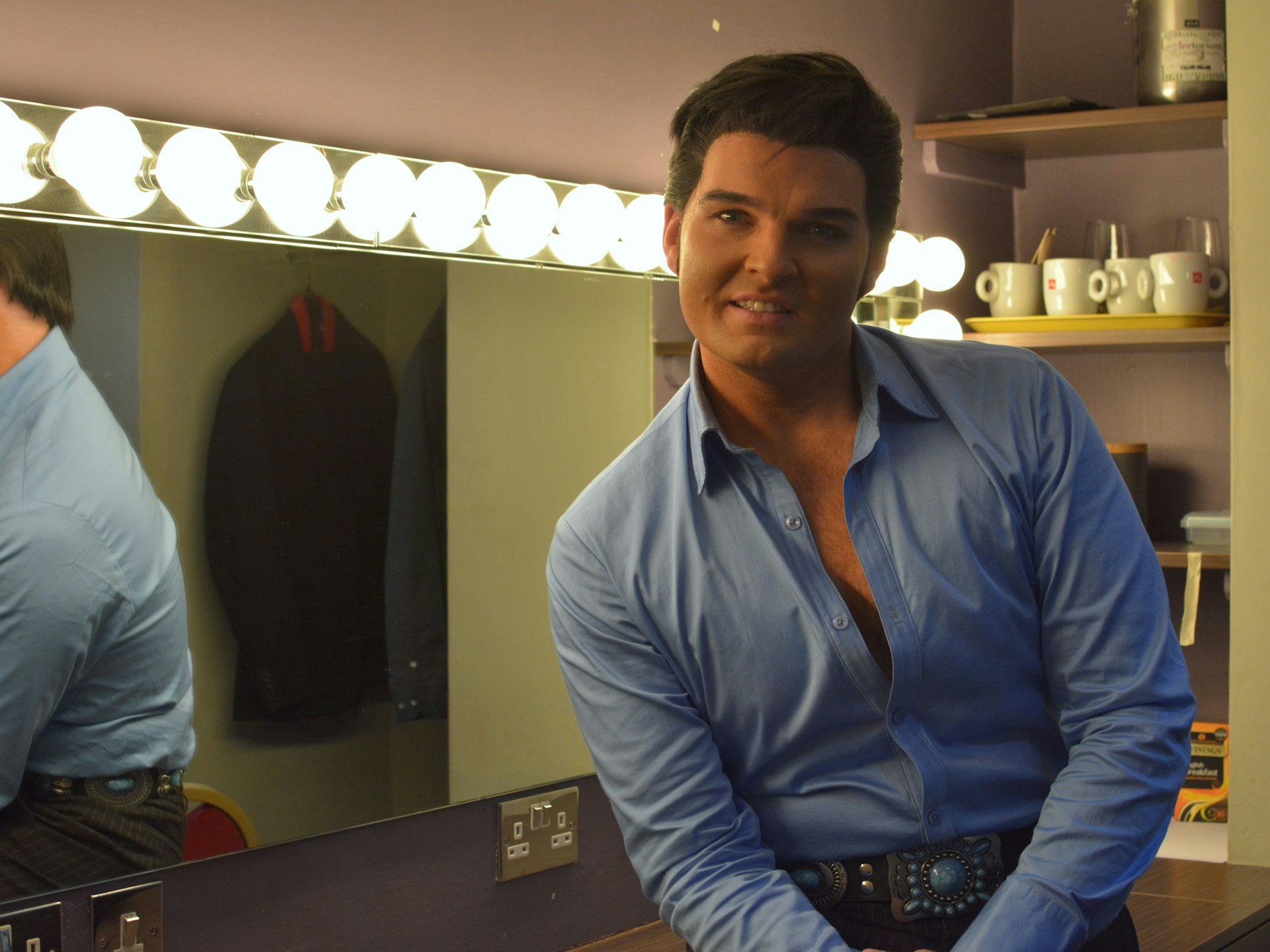 Ein Mann im Elvis-Look schaut vor einem Spiegel in die Kamera.