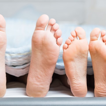 Füße eines Paares im Bett gucken von unter der Decke hervor