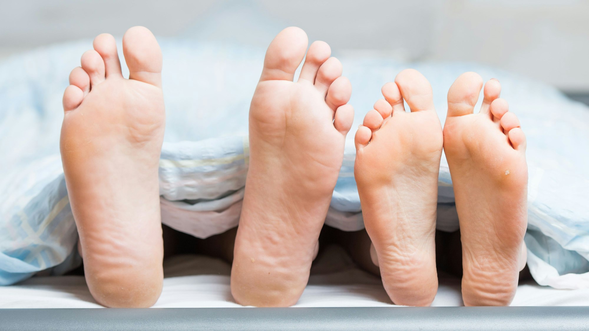 Füße eines Paares im Bett gucken von unter der Decke hervor