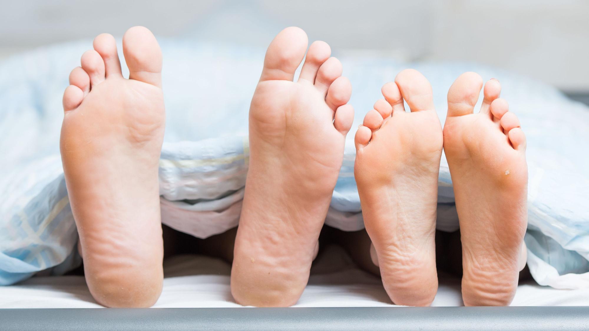 Füße eines Paares im Bett gucken von unter der Decke hervor