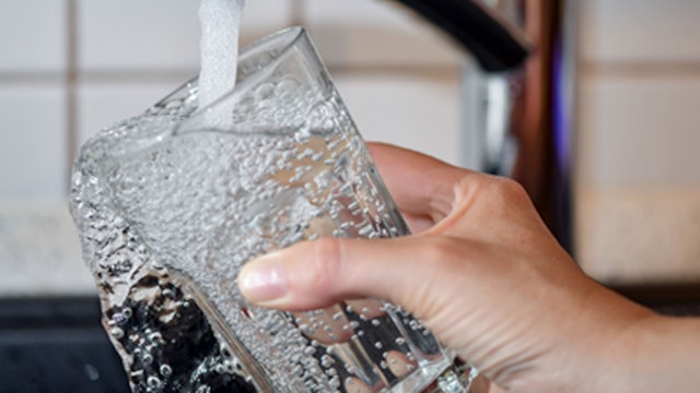 Eine Person hält ein Glas unter einen geöffneten Wasserhahn.