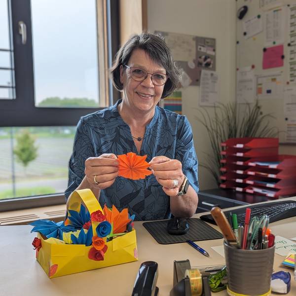 Schulleiterin Sabine Sommer in ihrem Büro. Vor sich auf dem Schreibtisch ein Korb mit bunten Papierblüten.