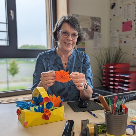 Schulleiterin Sabine Sommer in ihrem Büro. Vor sich auf dem Schreibtisch ein Korb mit bunten Papierblüten.
