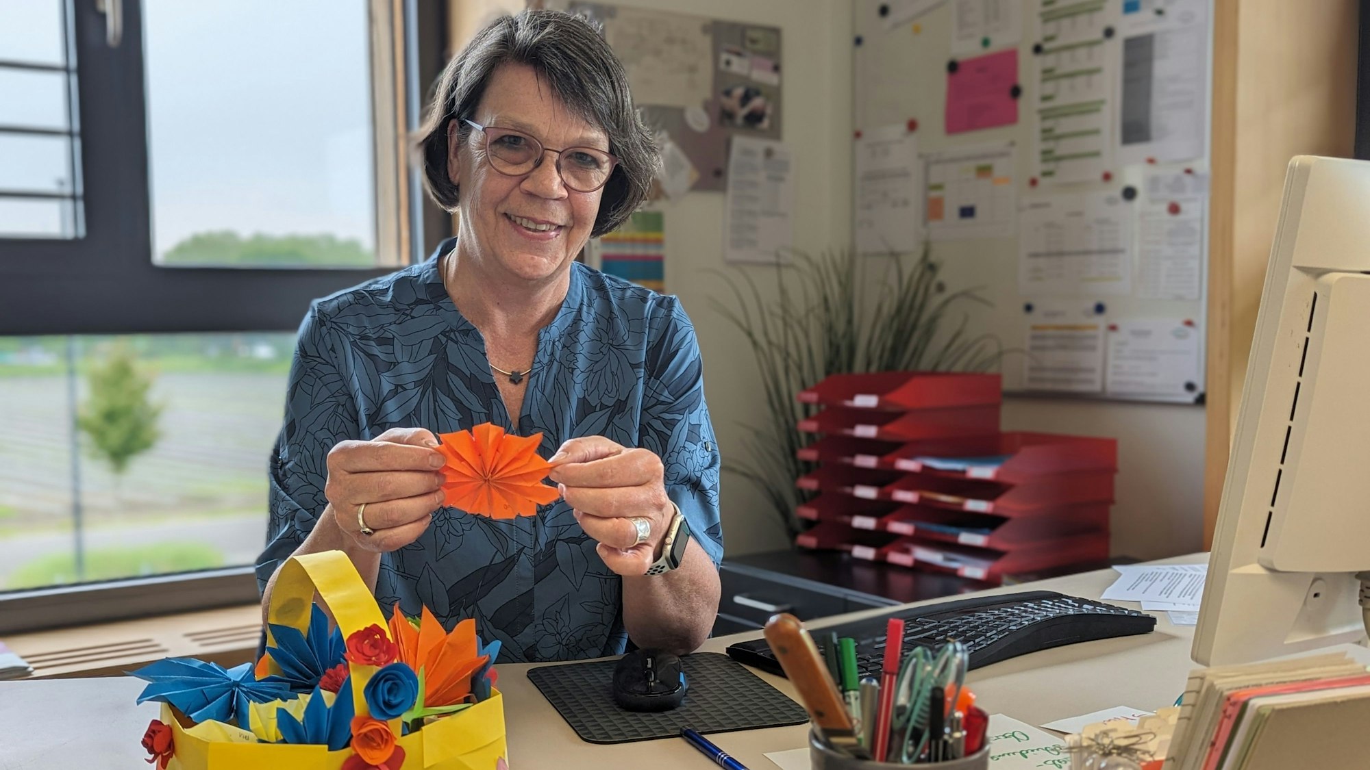 Schulleiterin Sabine Sommer in ihrem Büro. Vor sich auf dem Schreibtisch ein Korb mit bunten Papierblüten.