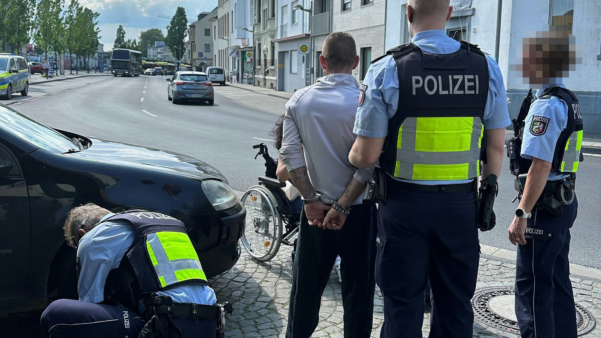 Drei Polizeibeamte stehen an einer Straße in Euskirchen. Sie haben einen Mann festgenommen, er ist mit Handschellen gefesselt.