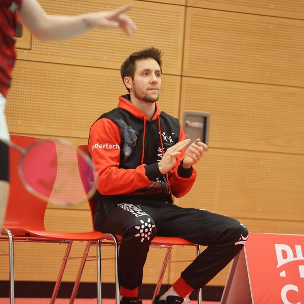 Blick auf einen Sportler, der auf einem Stuhl ein Badmintonspiel verfolgt.