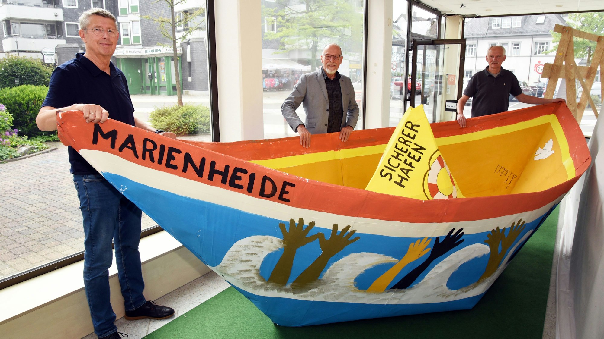 Werner Rosenthal, Gerd Fangmann und Friedel Bondke stehen an einem großen und bemalten Papierschiff.