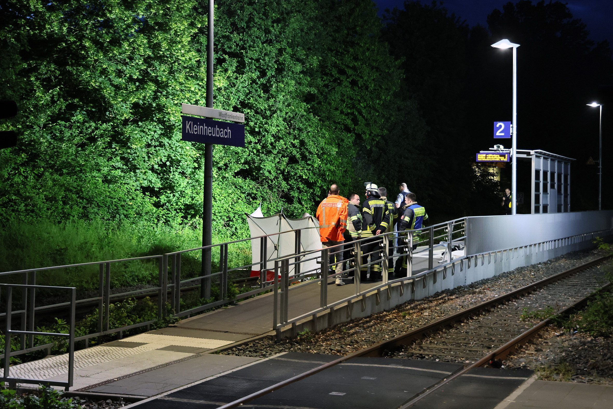 dpatopbilder - 18.05.2024, Bayern, Kleinheubach: Rettungskräfte stehen an einem Bahnsteig in Kleinheubach. Kleinheubach (dpa) - Zwei Männer sind bei einem Zugunglück in Unterfranken ums Leben gekommen. Die beiden 22- und 37-Jährigen seien am Samstagabend am Bahnhof in Kleinheubach (Landkreis Miltenberg) zwischen die Waggons eines anfahrenden Zugs geraten, dabei ins Gleisbett gefallen und tödlich verletzt worden, teilte die Polizei am Sonntag mit. Nach derzeitigem Ermittlungsstand hielten sich die Männer alleine am Bahnsteig auf. Foto: Ralf Hettler/dpa +++ dpa-Bildfunk +++