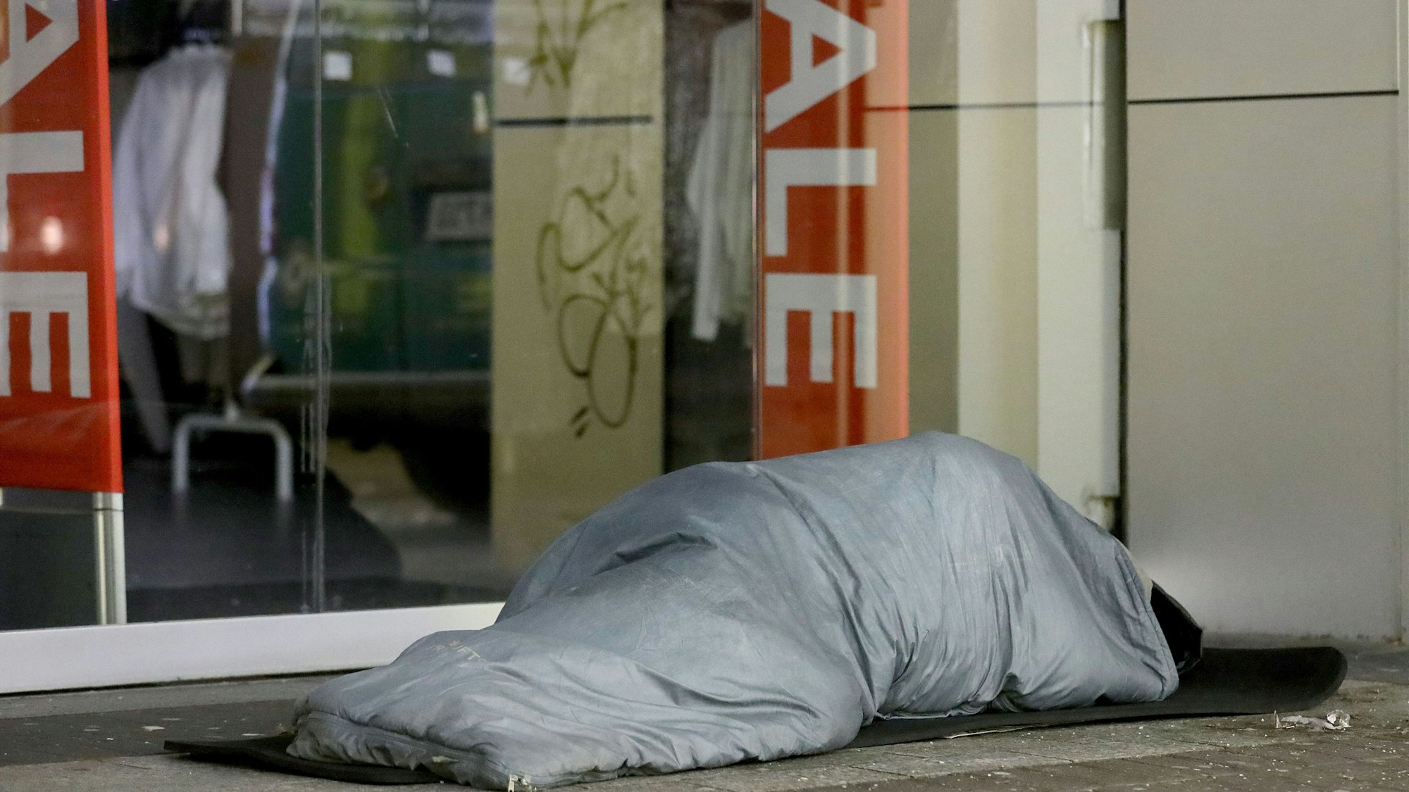 Ein Obdachloser schläft vor einem Geschäft in Köln.