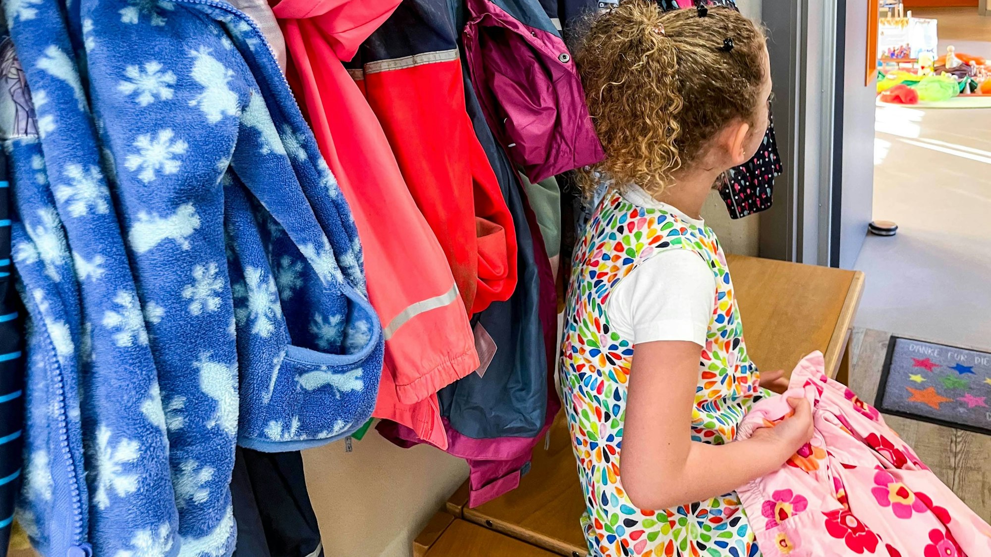 Ein Mädchen sitzt an der Garderobe einer Kindergartengruppe.
