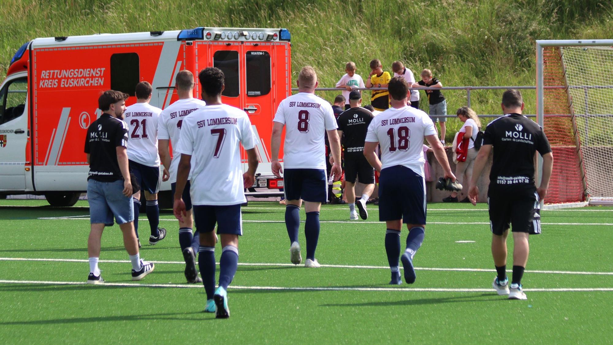 Fußballspieler gehen in Richtung eines Rettungswagens, der auf der Torauslinie steht.