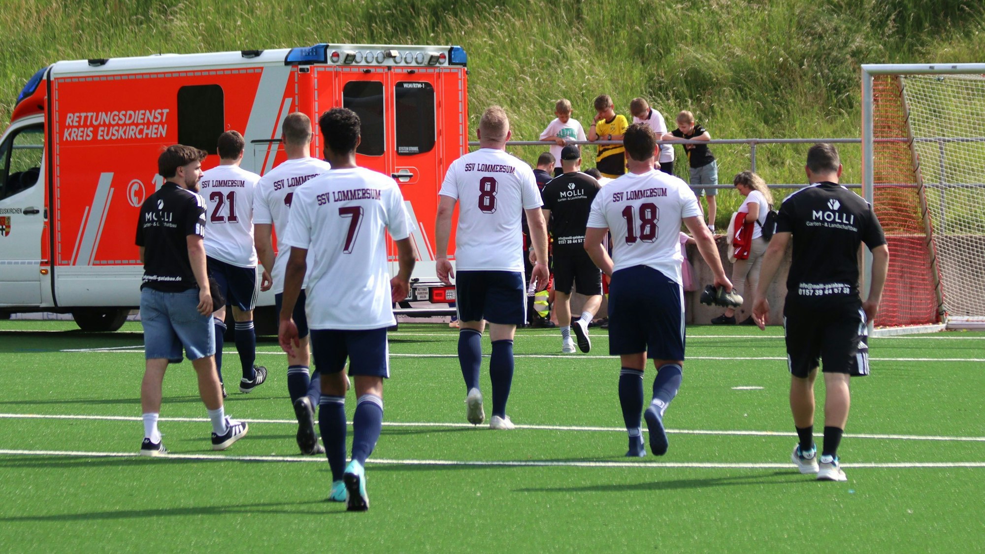 Fußballspieler gehen in Richtung eines Rettungswagens, der auf der Torauslinie steht.