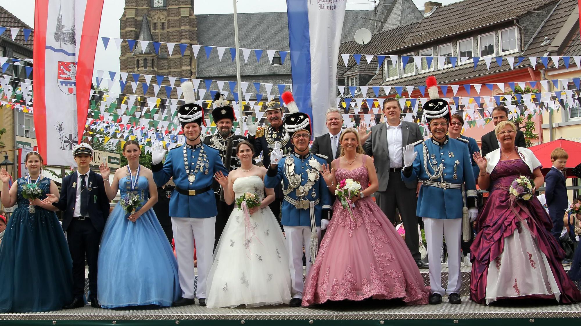 Eine Gruppe von Männern in Schützenuniform und Frauen in Ballkleidern nimmt auf einer Tribüne die Schützenparade ab.