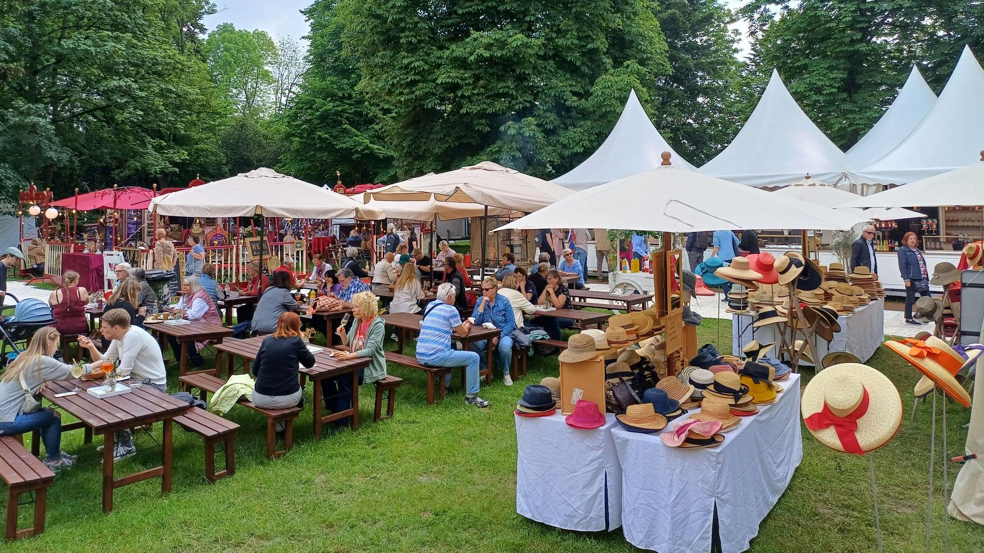 Menschen sitzen im Freien an Tischen leben Verkaufsständen.
