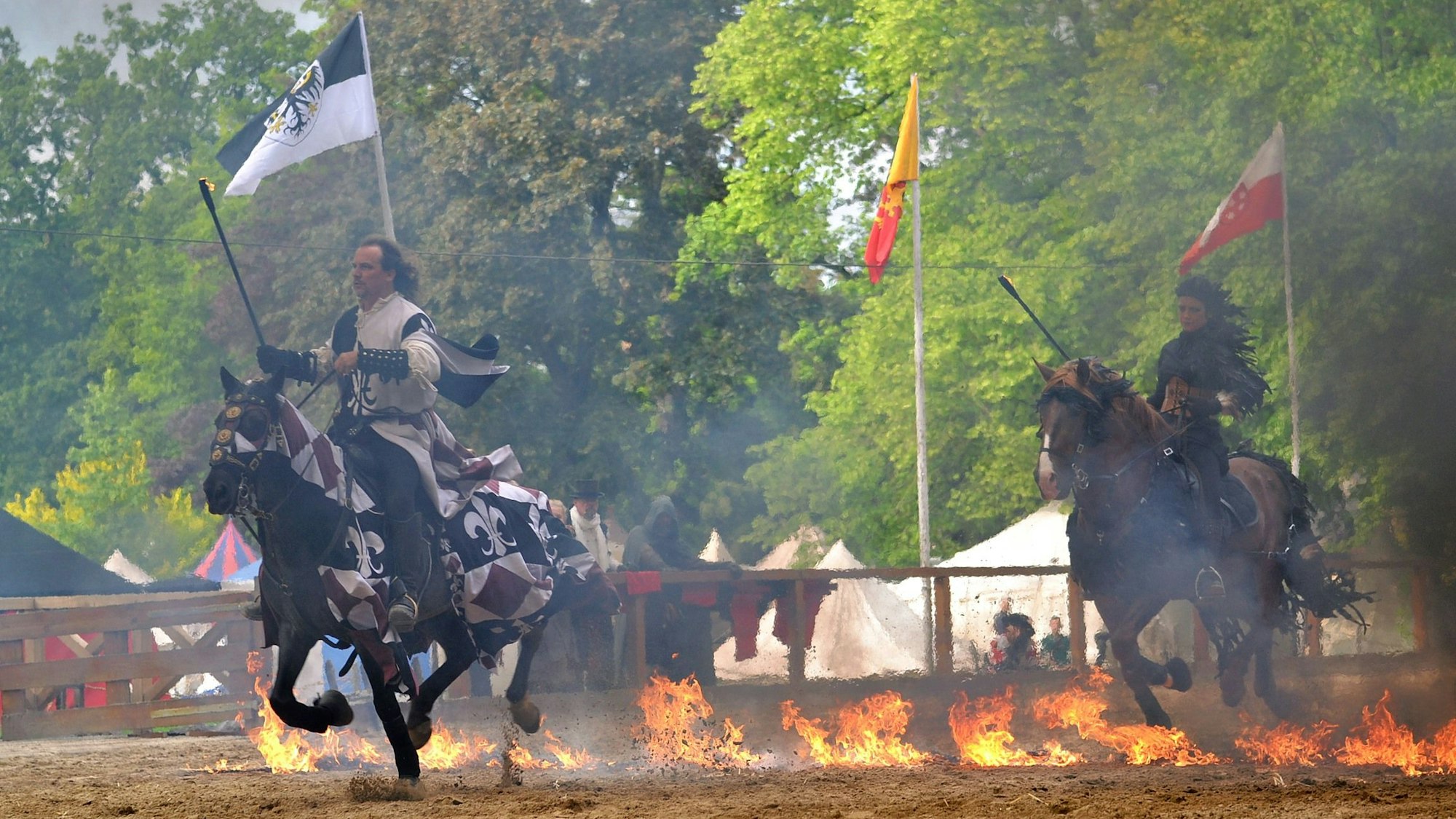 Ein Reiter und eine Reiterin traben mittelalterlich verkleidet mit ihren Pferden durch eine Feuerlinie.