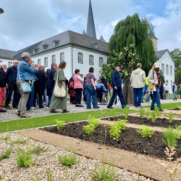 Eine große Gruppe von Besucherinnen und Besuchern geht an den Beeten vor der Abtei Brauweiler vorbei.