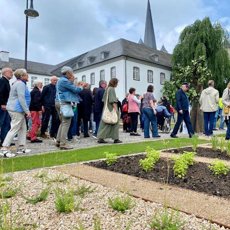 Eine große Gruppe von Besucherinnen und Besuchern geht an den Beeten vor der Abtei Brauweiler vorbei.