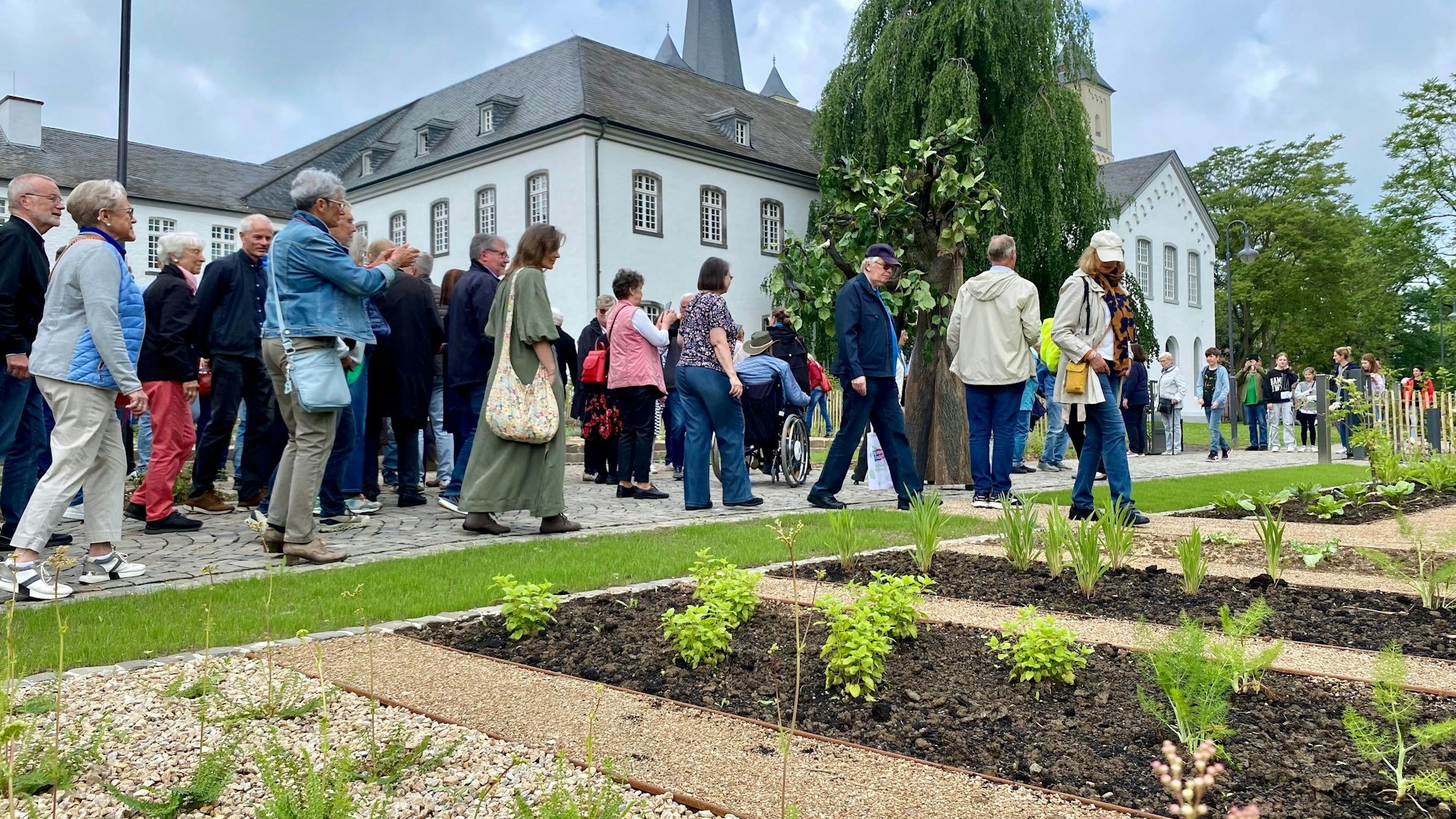 Eine große Gruppe von Besucherinnen und Besuchern geht an den Beeten vor der Abtei Brauweiler vorbei.