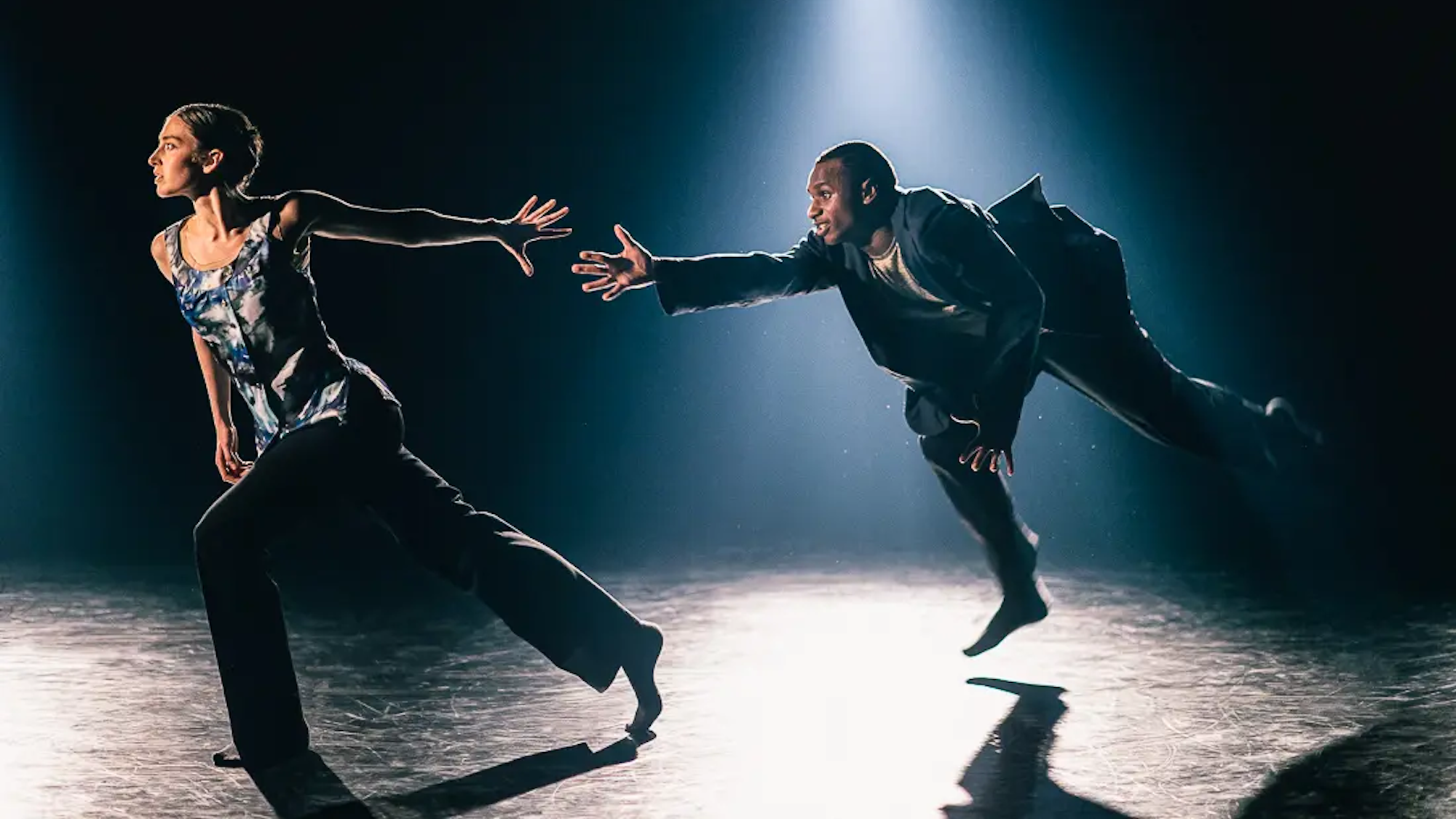 Eine Tänzerin und ein Tänzer versuchen einander im Laufen bei den Händen zu greifen.