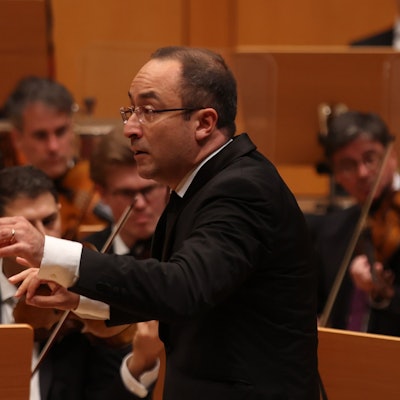 Riccardo Minasi trägt einen Frack und dirigiert ein Orchester.