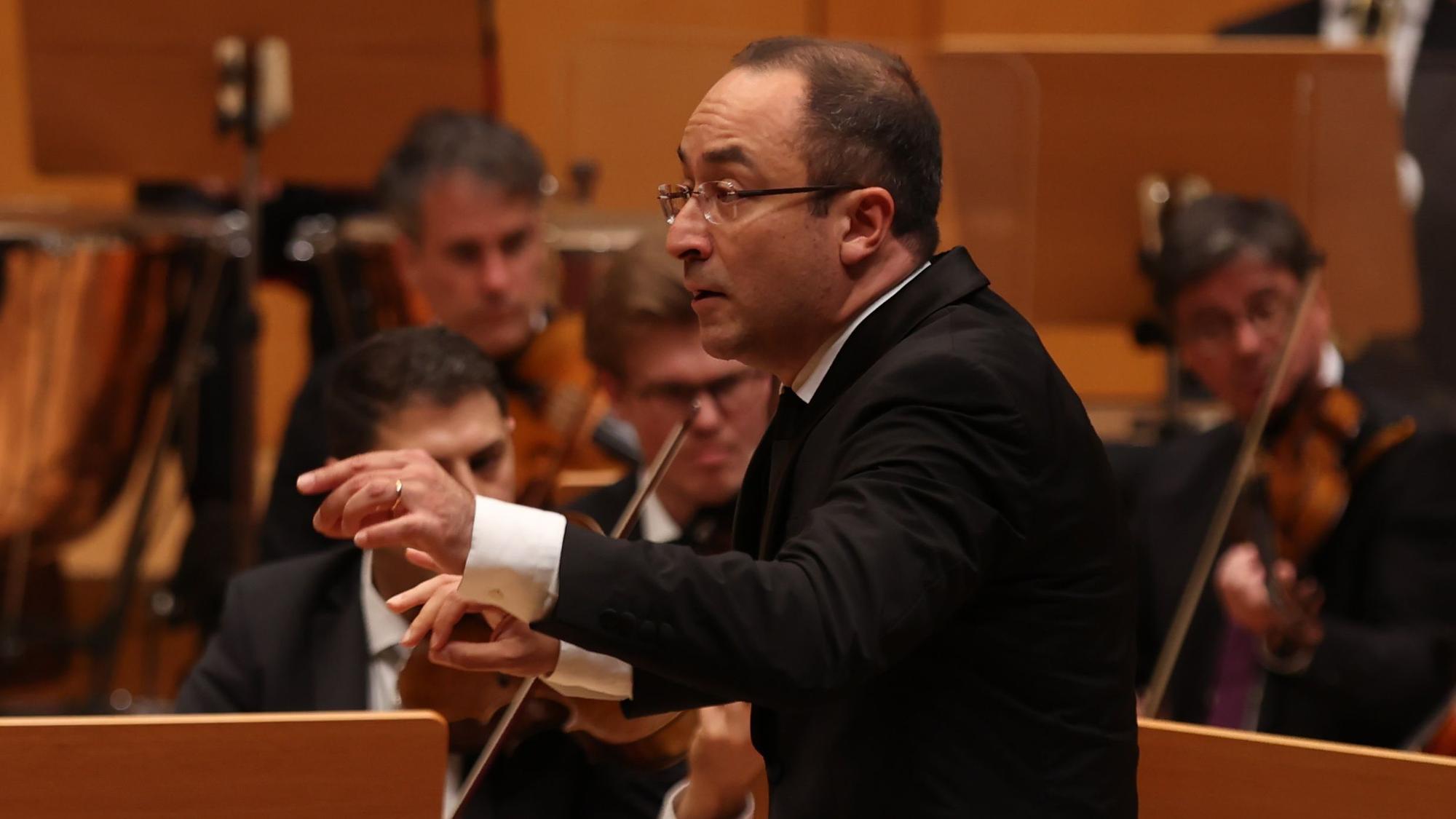 Riccardo Minasi trägt einen Frack und dirigiert ein Orchester.
