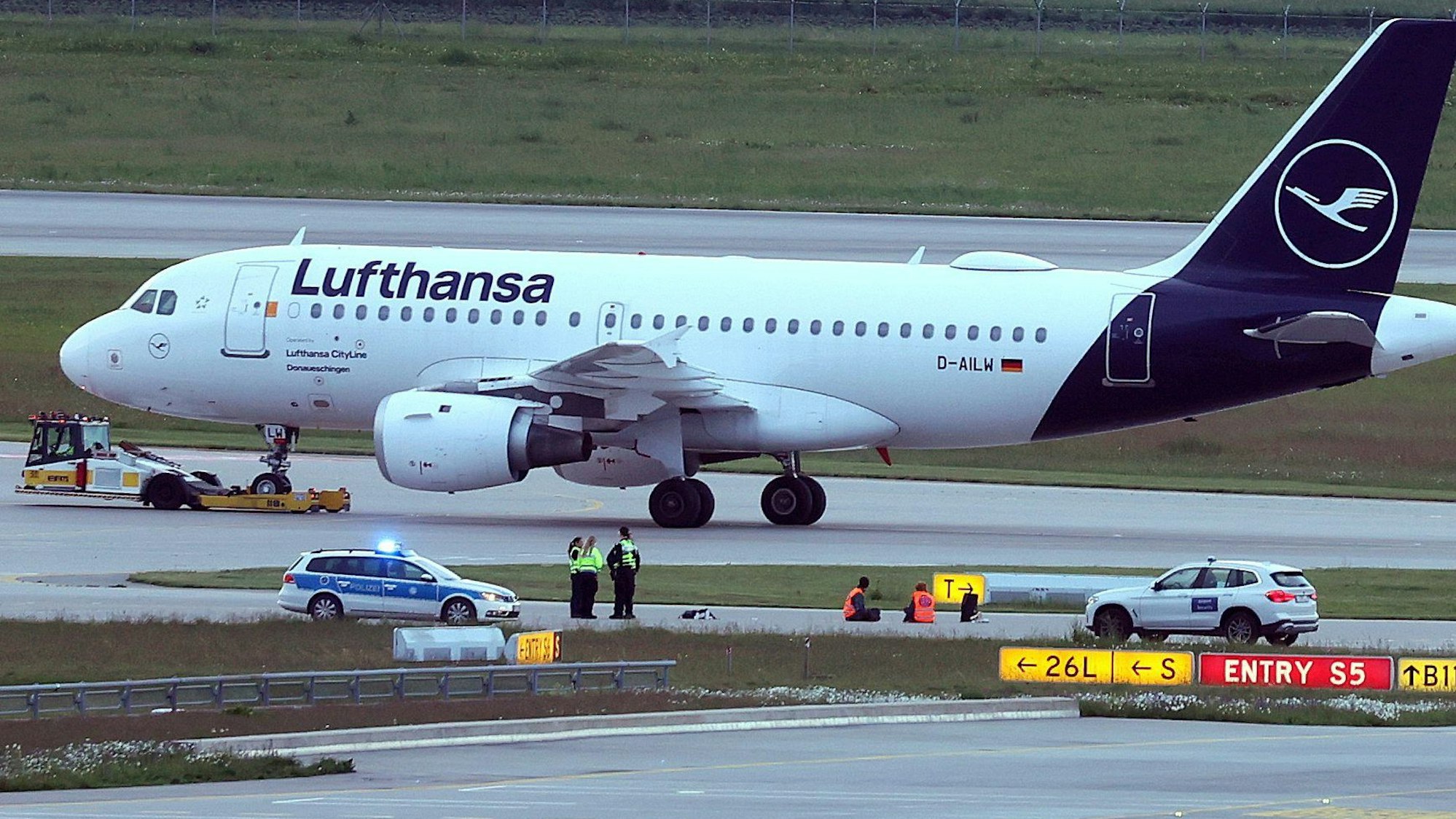 18.05.2024, Bayern, München: Zwei Aktivisten haben sich auf einer Zufahrt für Start- und Landebahnen am Flughafen Franz-Josef-Strauß festgeklebt. Klimaschutzaktivisten haben am frühen Samstagmorgen den Münchner Flughafen lahmgelegt. Die Aktivisten waren in den inneren Bereich des Airport-Geländes gelangt. Mitglieder der sogenannten Letzten Generation hatten nach eigenen Angaben geplant, auf das Gelände des Flughafens zu gelangen, um mindestens eine der beiden Start- und Landebahnen zu blockieren. Foto: Karl-Josef Hildenbrand/dpa +++ dpa-Bildfunk +++