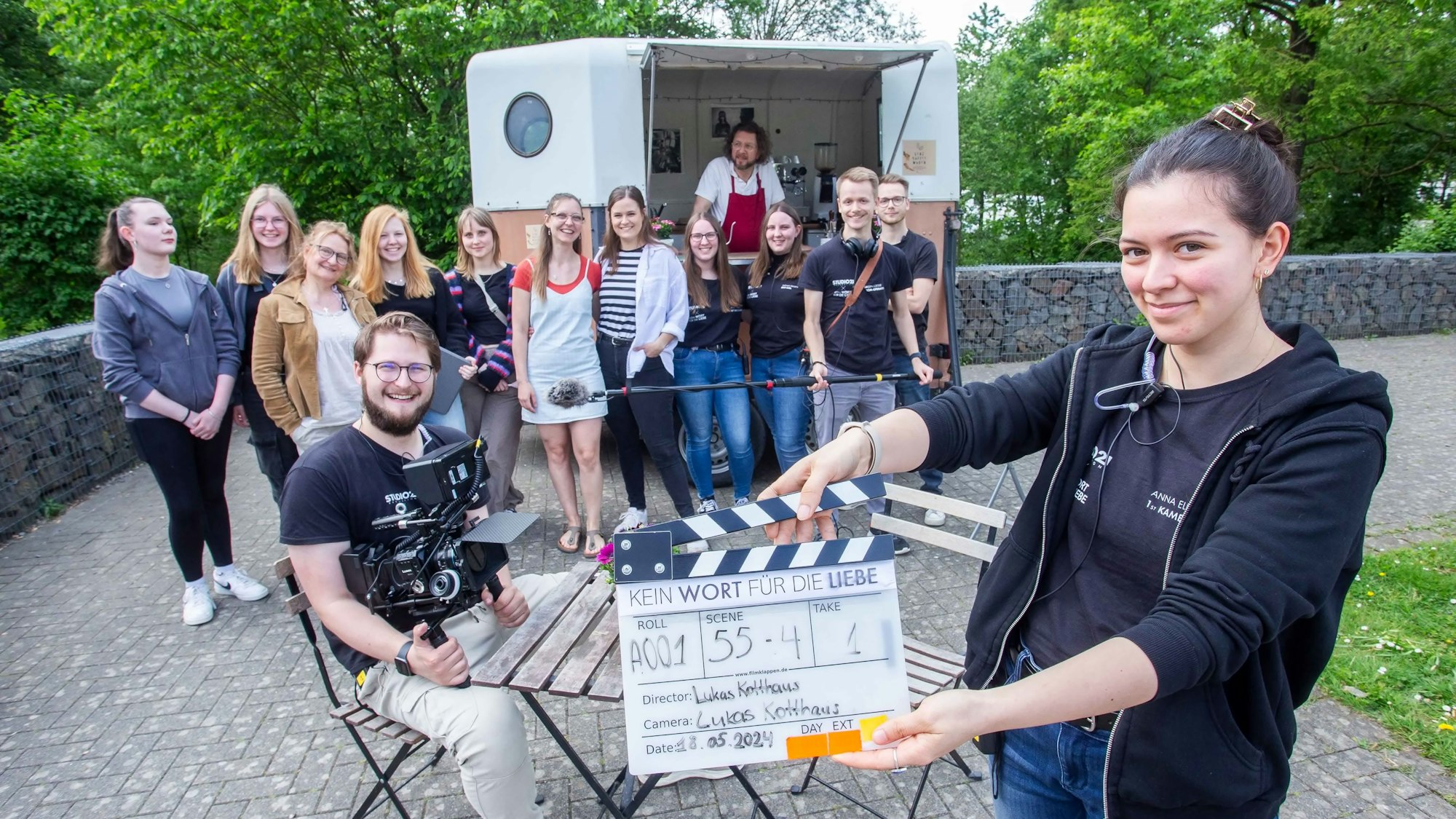 Einblick bei den Dreharbeiten zu „Kein Wort für die Liebe.“ Eine Gruppe steht im Hintergrund. Im Vordergrund steht eine Frau mit einer Szenenklappe.