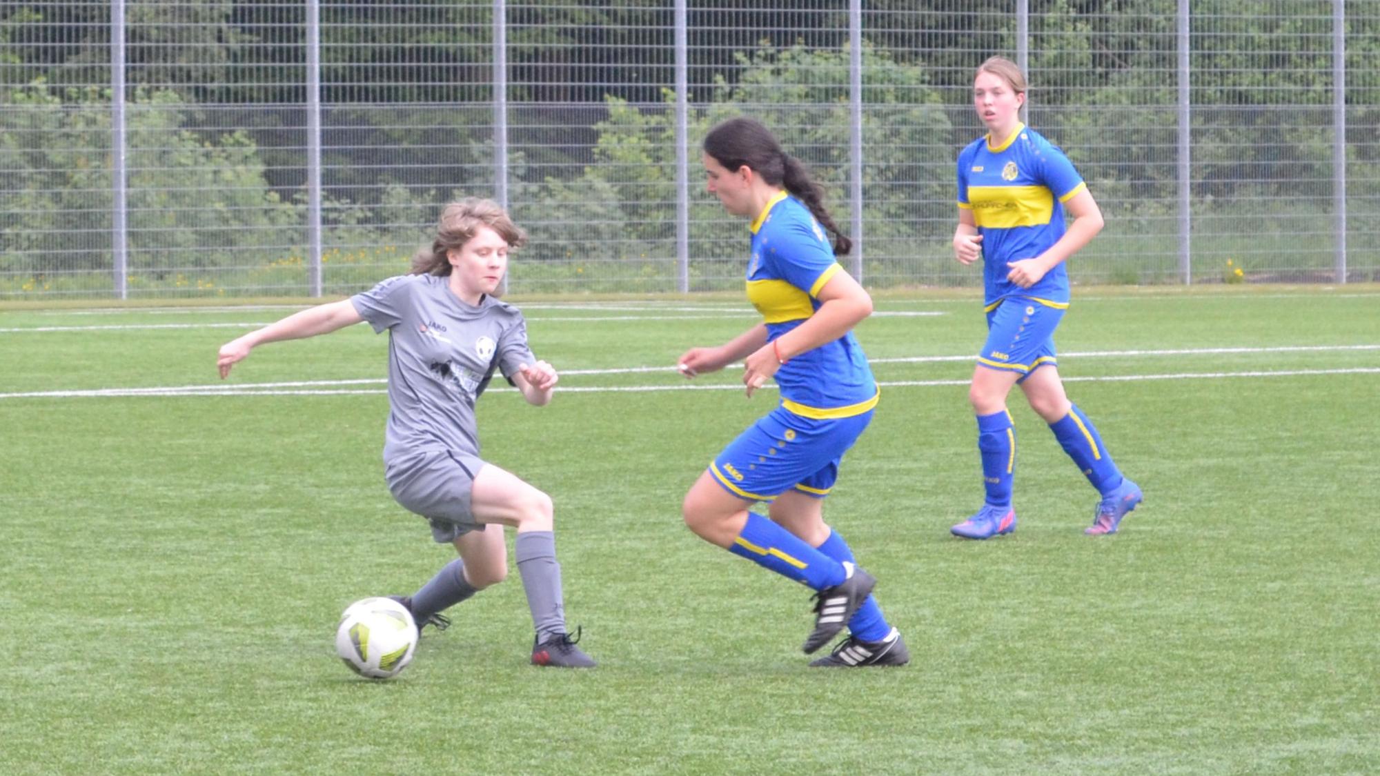 Spielsituation zweier Mädchenteams auf einem Fußballplatz.