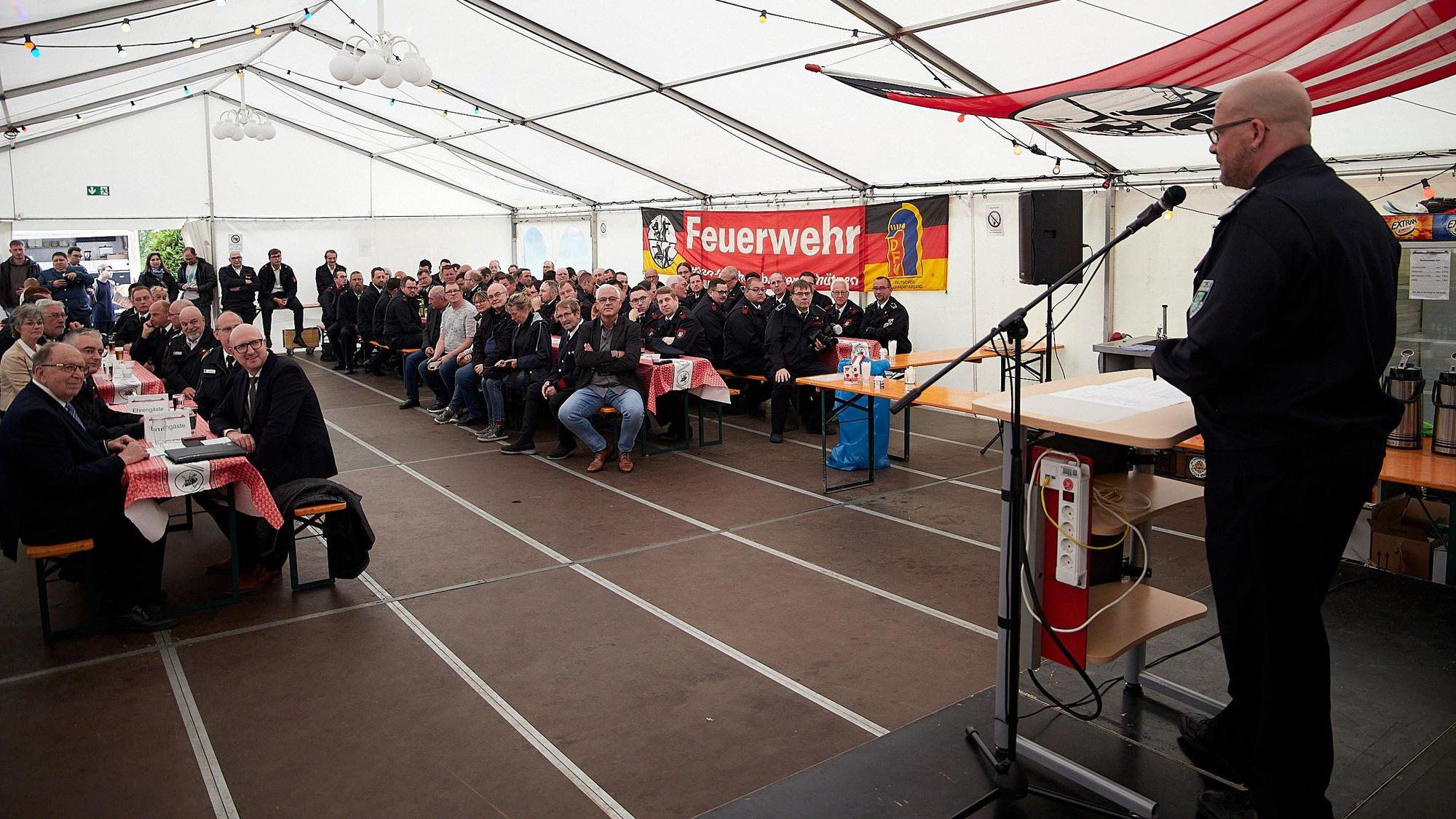 Das Bild zeigt einen Blick ins Festzelt. Auf der Bühne steht am Mikrofon ein Redner.