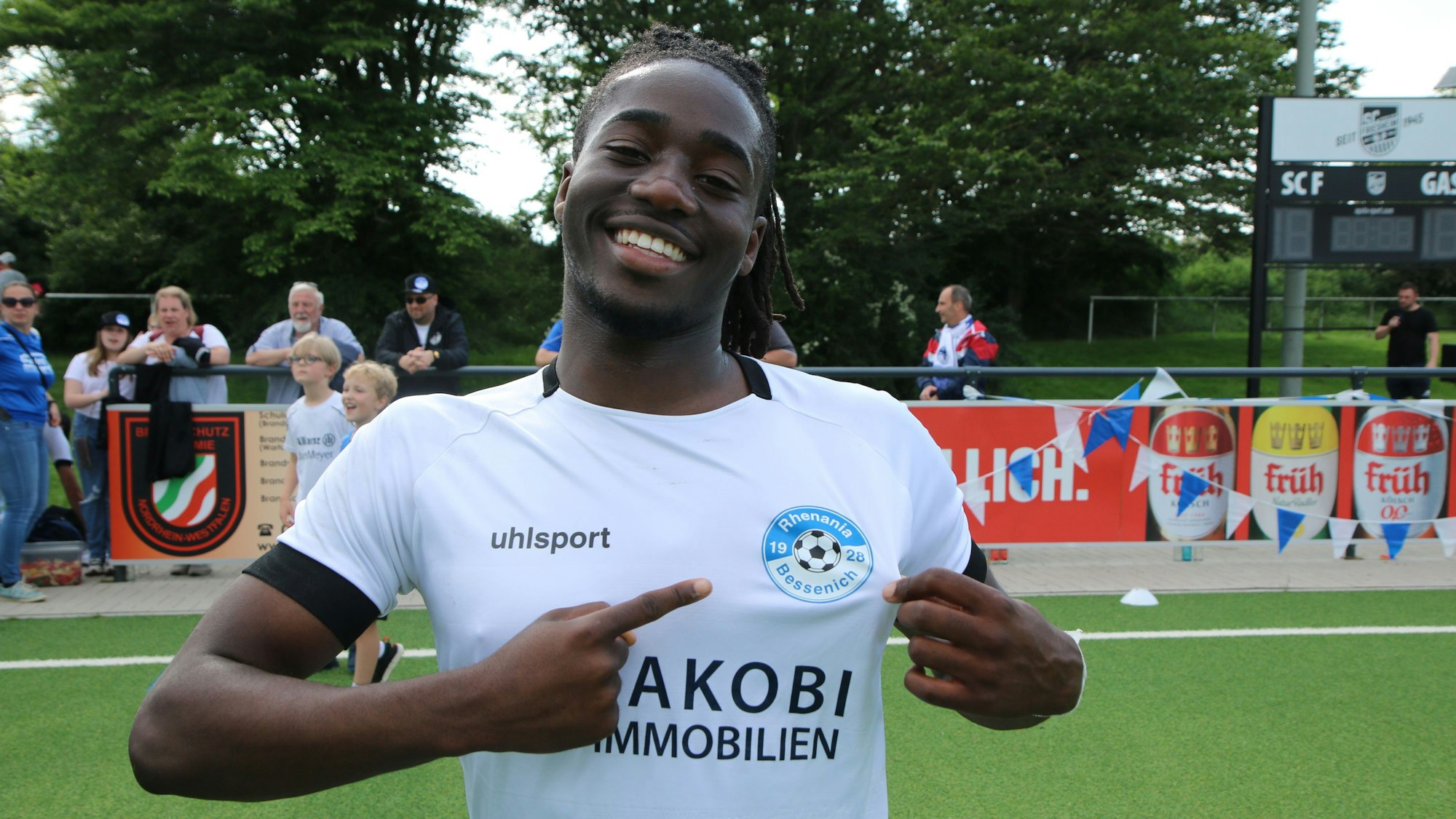 Samson Sayongo zeigt mit ausgestrecktem Finger auf das Bessenich-Logo.