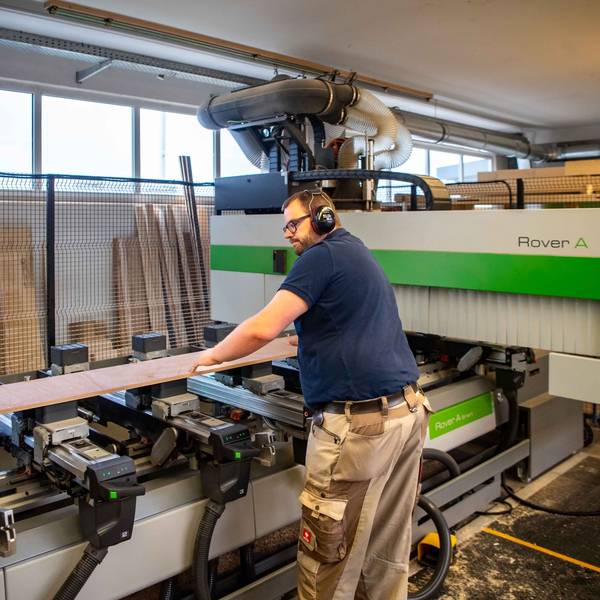 Das Bild zeigt den Schreiner an der Maschine. Er hat gerade ein Brett platziert, das nun bearbeitet werden soll.