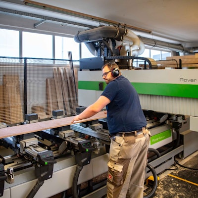 Das Bild zeigt den Schreiner an der Maschine. Er hat gerade ein Brett platziert, das nun bearbeitet werden soll.