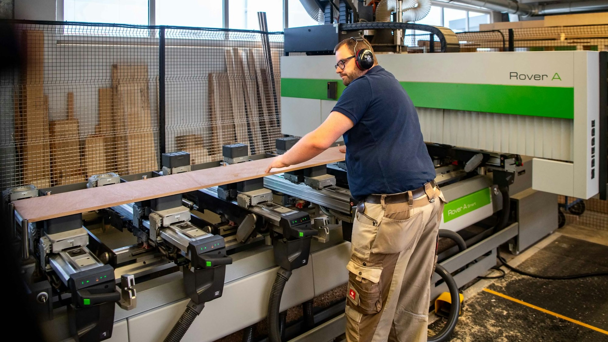 Das Bild zeigt den Schreiner an der Maschine. Er hat gerade ein Brett platziert, das nun bearbeitet werden soll.