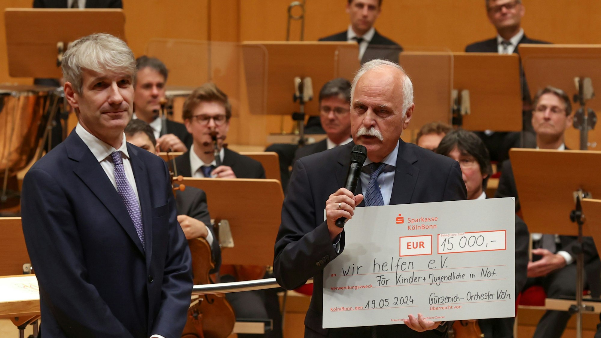 Der Geschäftsführende Direktor des Gürzenich-Orchesters Stefan Englert überreicht Karl-Heinz Goßmann vom „wir helfen“-Vorstand auf der Bühne der Kölner Philharmonie einen symbolischen Scheck über 15.000 Euro