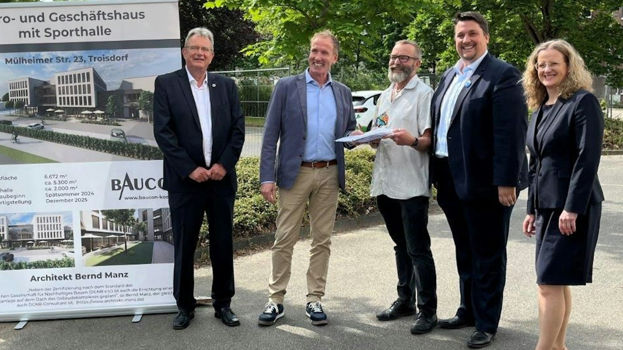 Vier Männer und eine Frau stehen neben einem Aufsteller mit Bildern von einem Wohn- und Geschäftshaus.