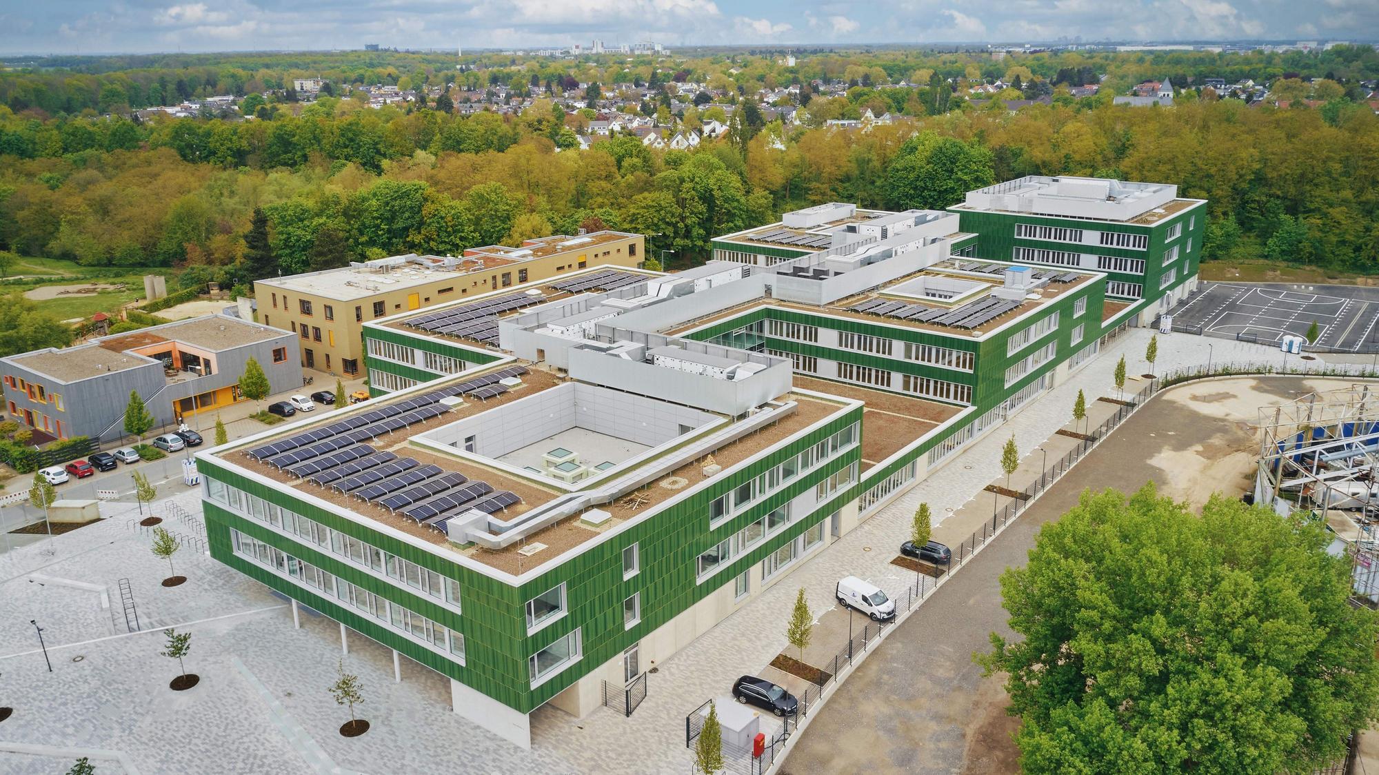Ein großes dreistöckiges Flachdach-Schulgebäude ist aus der Luft zu sehen.