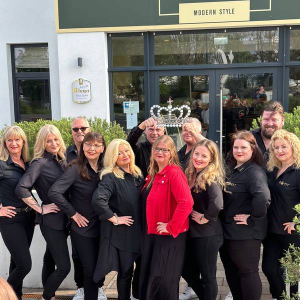 Eine Gruppe von schwarz gewandeten Damen und Herren, in der Mitte die künftige Prinzessin in rotem Blazer und Krone, die von zwei Männern über ihrem Kopf gehalten wird.