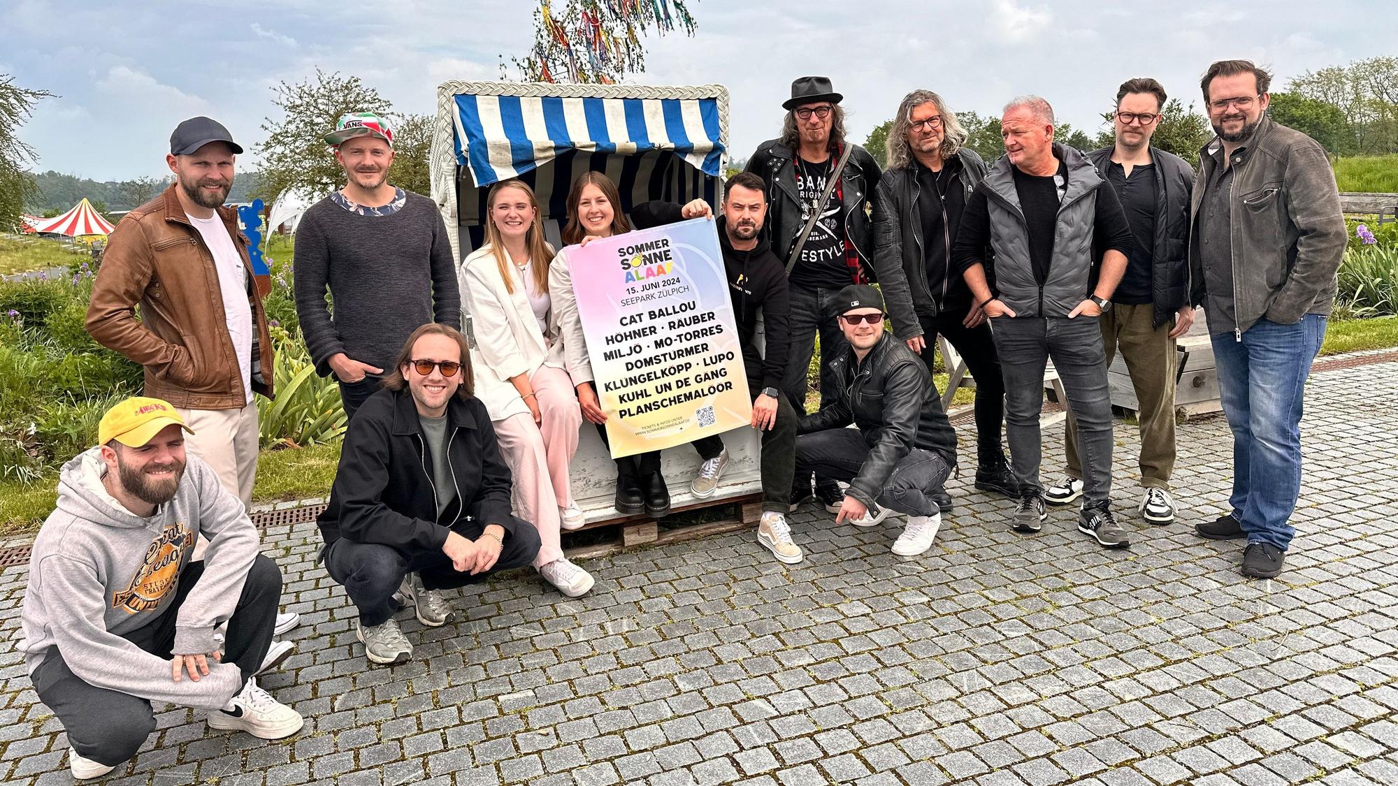 Die Veranstalter von Sommer Sonne Alaaf sowie die Bands Lupo und Domstürmer posieren vor einem Maibaum im Seepark.