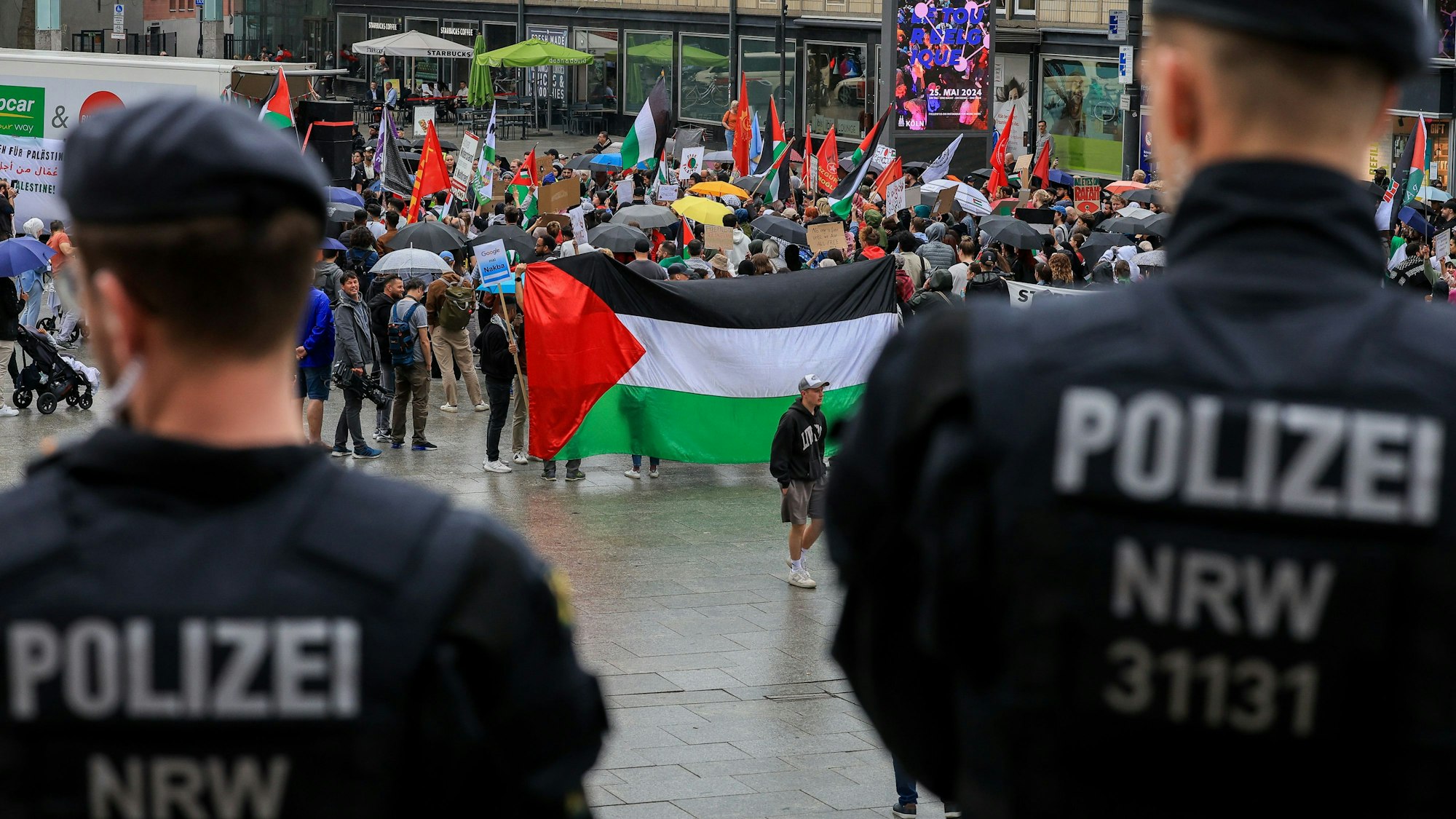 Propalästinensische Demonstranten stehen am Kölner Bahnhofsvorplatz, davor stehen zwei Polizisten.