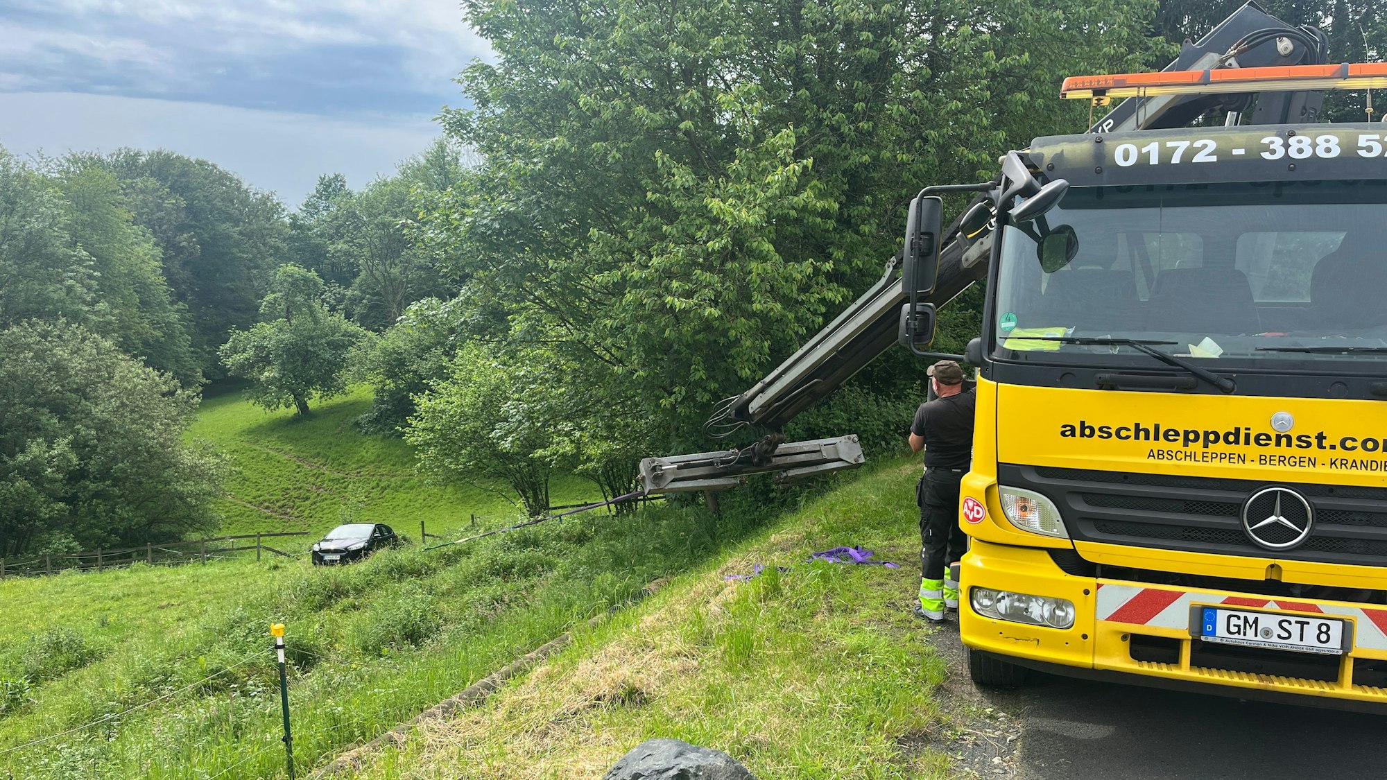 Ein Abschleppunternehmer zieht mit seinem Kranfahrzeug das Auto über den Hang nach oben.