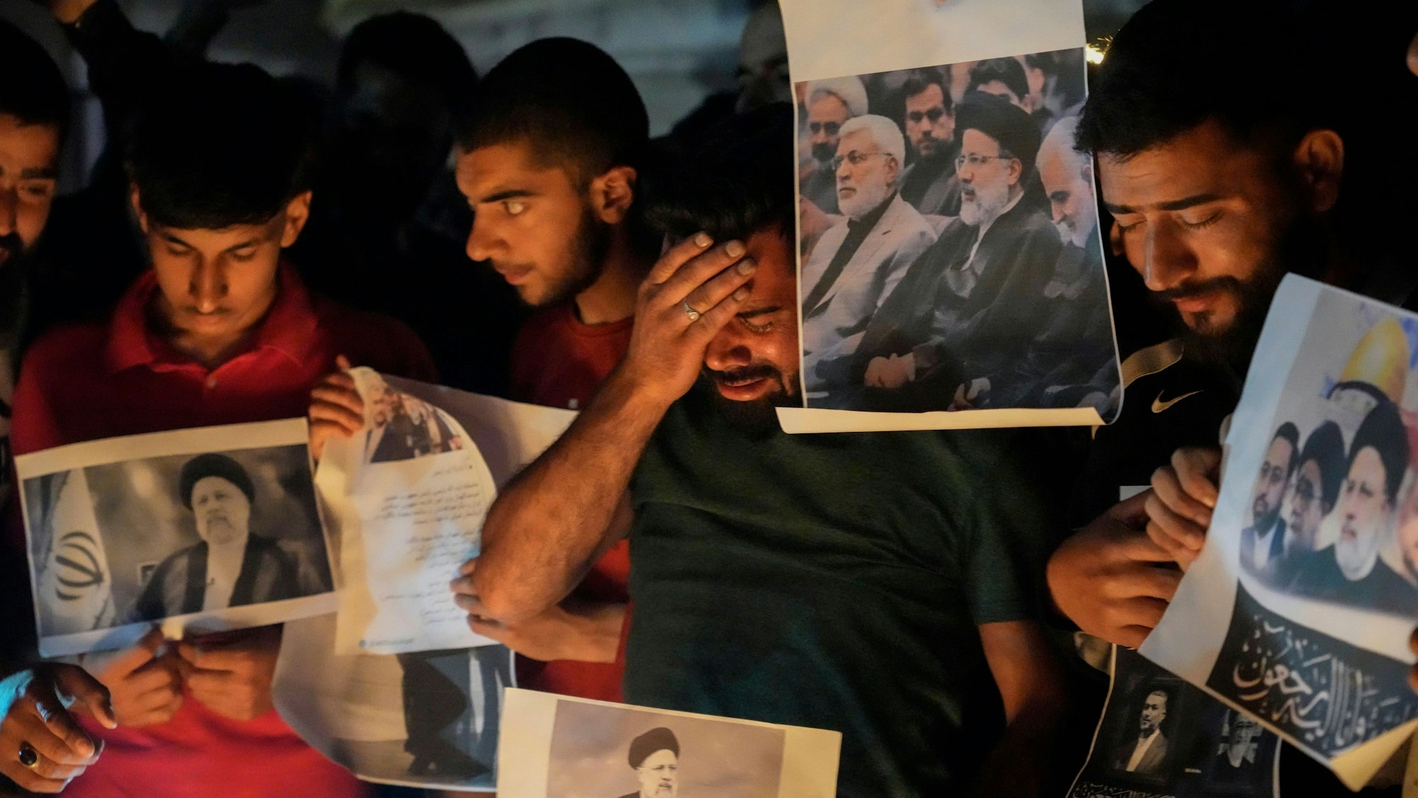 Ein schiitischer Muslim weint, während er Fotos des iranischen Präsidenten Ebrahim Raisi und anderer führender Persönlichkeiten während einer Mahnwache hält.