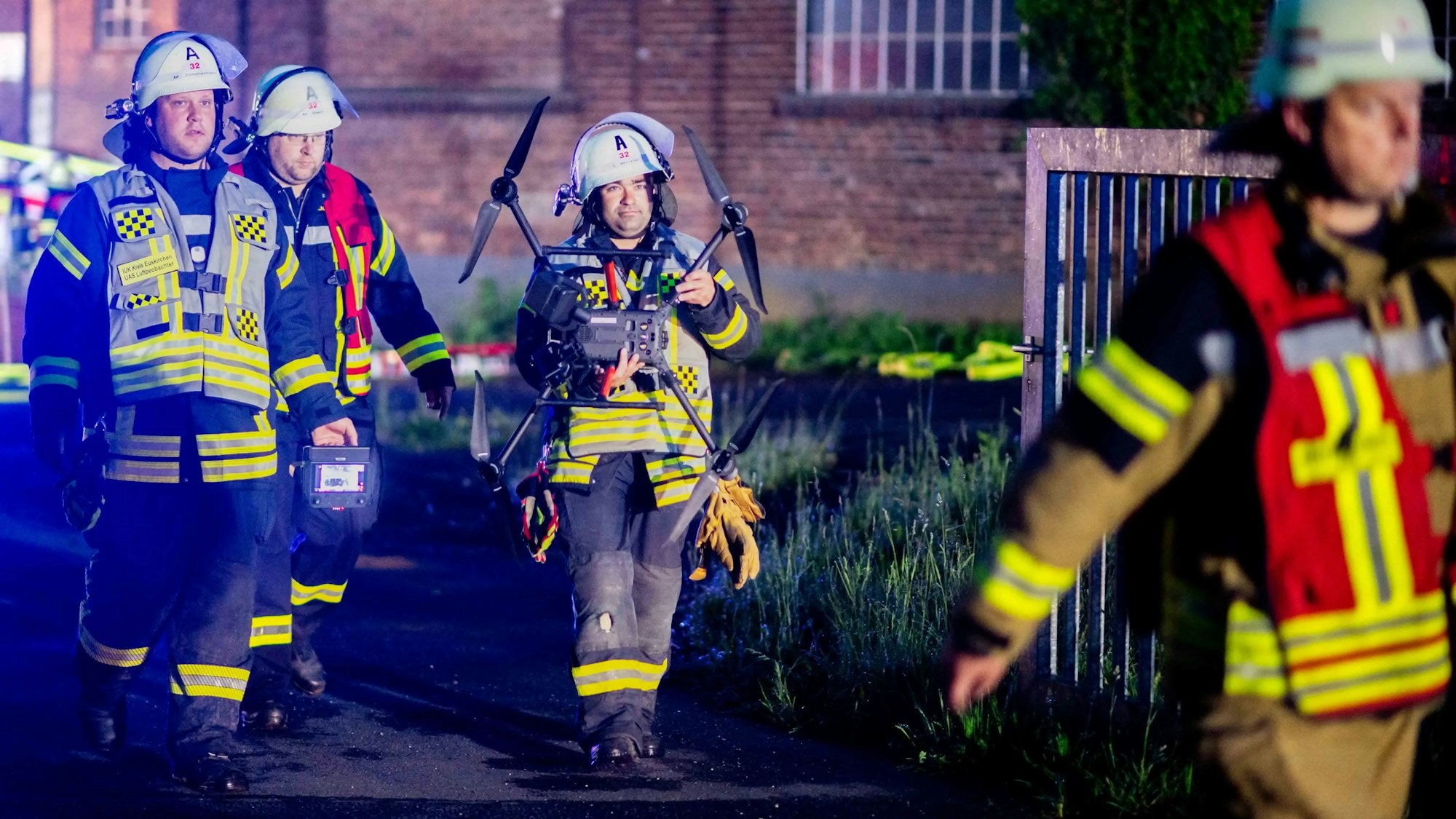 Vier Feuerwehrleute verlassen das Werksgelände. Einer von ihnen trägt die Drohne mit beiden Händen.