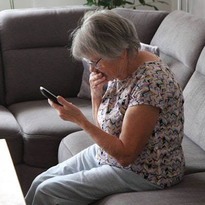 Eine Frau sitzt auf dem Sofa, mit einem schnurlosen Telefon in der Hand.
