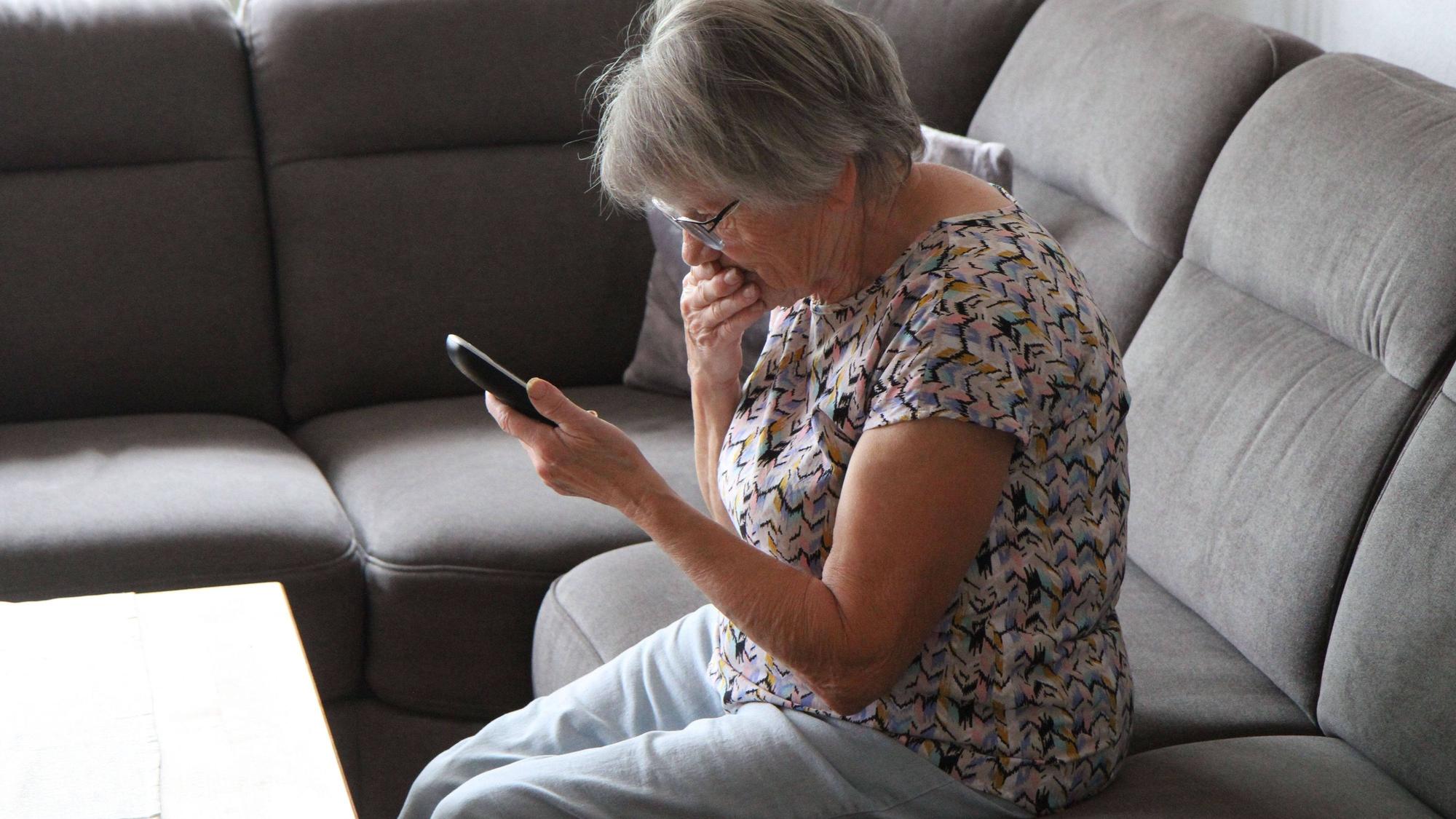 Eine Frau sitzt auf dem Sofa, mit einem schnurlosen Telefon in der Hand.