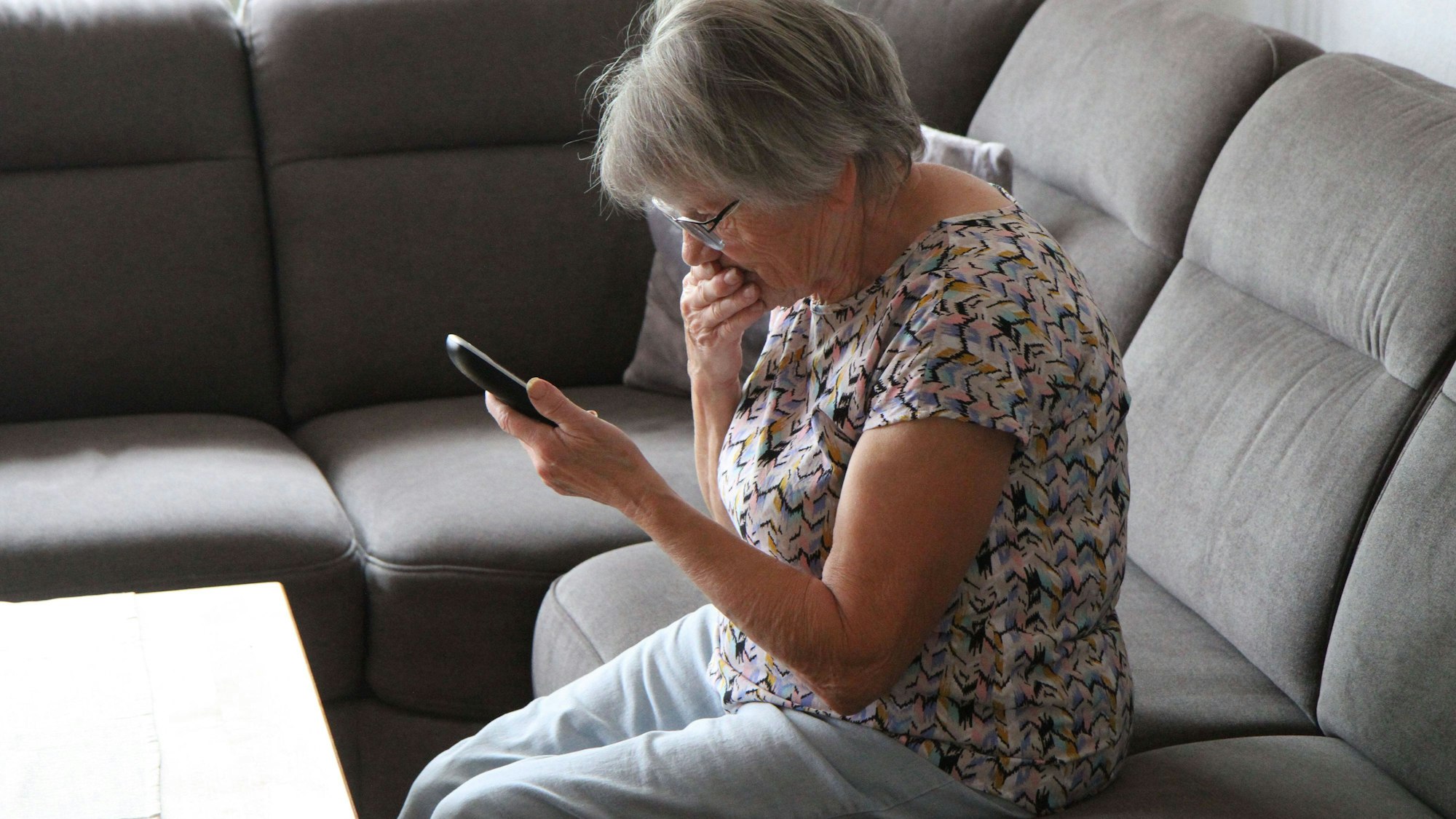 Eine Frau sitzt auf dem Sofa, mit einem schnurlosen Telefon in der Hand.